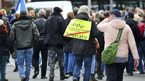 Auf einer Kundgebung von Kritikern der staatlichen Corona-Maßnahmen in Wiesbaden trägt ein Teilnehmer ein Plakat, das einem Ortseingangsschild nachempfunden ist. Aufschrift: "Sie kommen in Diktatur - Sie verlassen Demokratie".