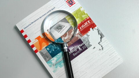 Auf dem Bild sieht man einen gedruckten Verfassungsschutzbericht auf dem eine Lupe liegt