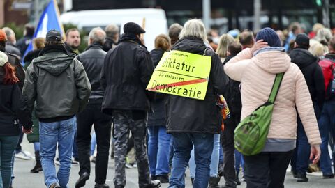 Auf einer Kundgebung von Kritikern der staatlichen Corona-Maßnahmen in Wiesbaden trägt ein Teilnehmer ein Plakat, das einem Ortseingangsschild nachempfunden ist. Aufschrift: "Sie kommen in Diktatur - Sie verlassen Demokratie".