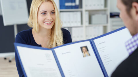 Bewerbungsgespräch - Zwei Menschen sitzen sich gegenüber, wobei eine Person eine Bewerbungsmappe hält