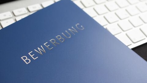 Auf der Abbildung sieht man eine blaue Bewerbungsmappe auf einer Computertastatur liegen
