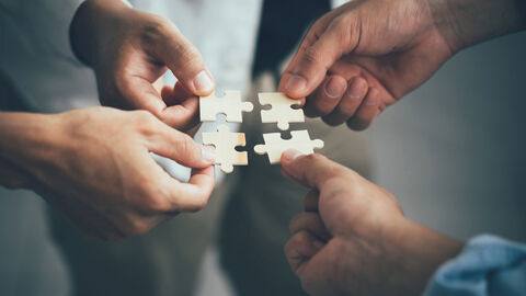 Auf dem Bild sieht man vier Hände, die Puzzlestücke zusammenführen - Symbolbild für Aufgaben und Zusammenarbeit