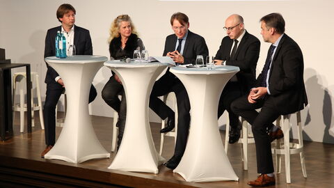 Julian Junk, Ine Dippmann, Moderator Thomas Kreutzmann, Sinan Selen und Lars Otte (von links nach rechts) sitzen während der Podiumsdiskussion auf der Bühne des Museum Wiesbaden hinter weißen Stehtischen