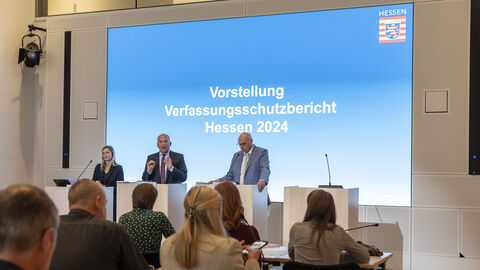 LfV-Präsident Bernd Neumann, Innenminister Roman Poseck und die Pressesprecherin des Innenministeriums bei der Vorstellung des Jahresberichts 2024 des LfV Hessen