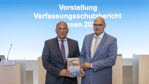 Innenminister Roman Poseck und der Präsident des LfV Hessen Bernd Neumann präsentieren den Jahresbericht 2024 des Landesamts für Verfassungsschutz Hessen und halten ein Exemplar in die Kamera